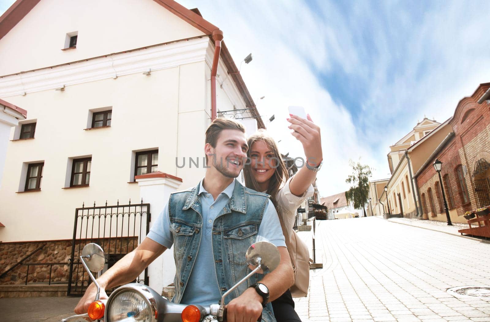Happy couple on scooter making selfie photo on smartphone outdoors by tsyhun