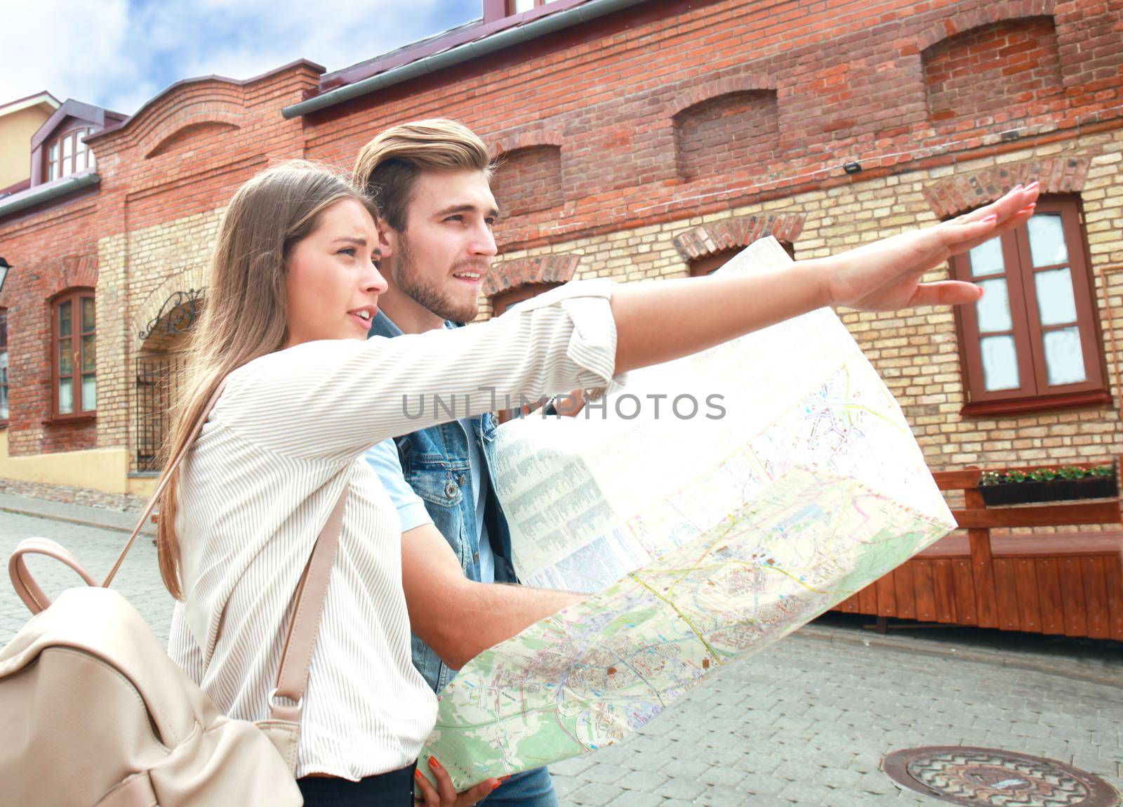 Happy couple walking outdoors sightseeing and holding a map. by tsyhun