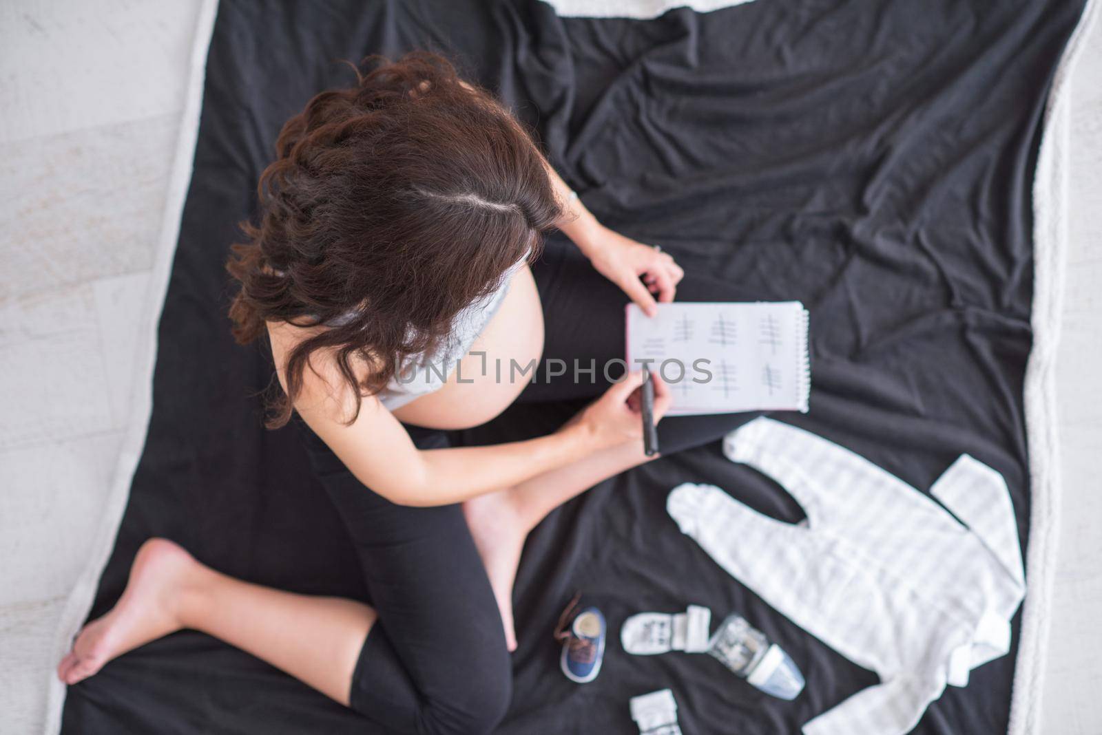 top view of pregnant woman checking list of baby clothes by dotshock