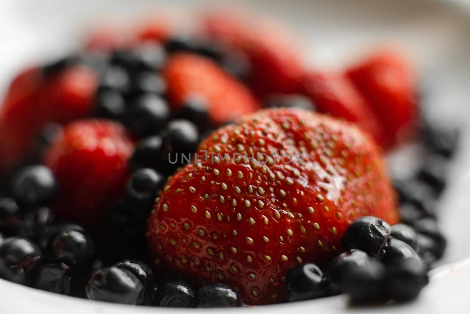 Picture of fresh berries in a white ceramic plate on grey background