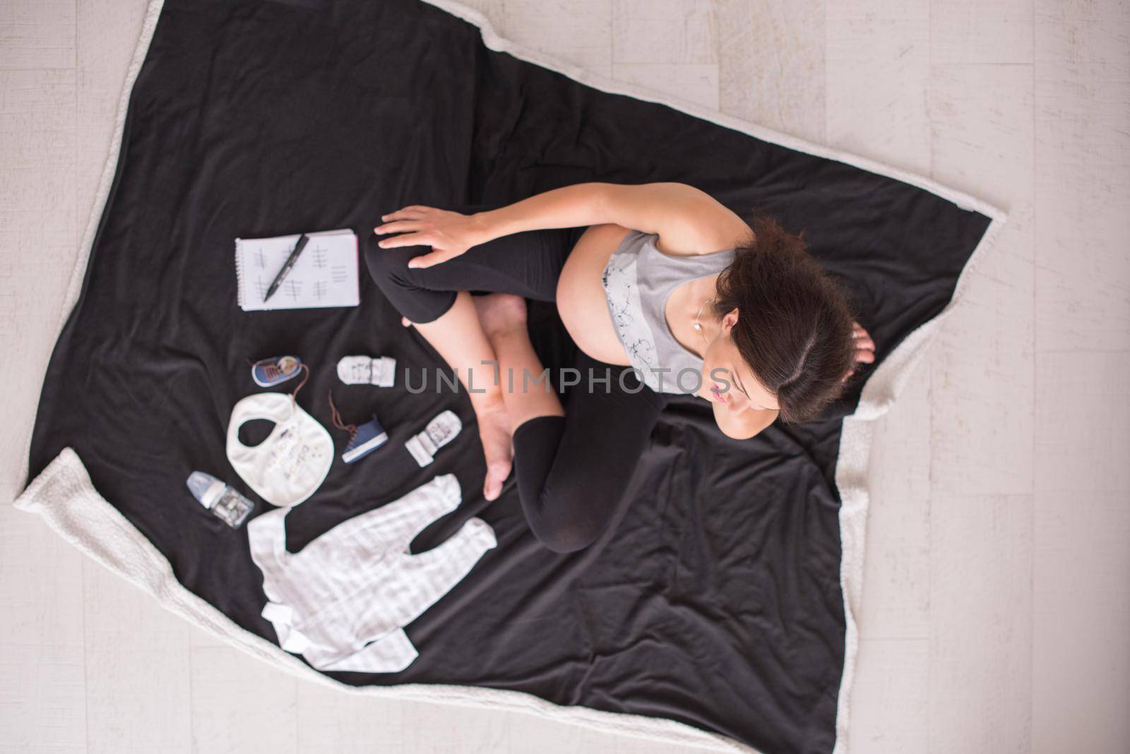 top view of pregnant woman checking list of baby clothes by dotshock