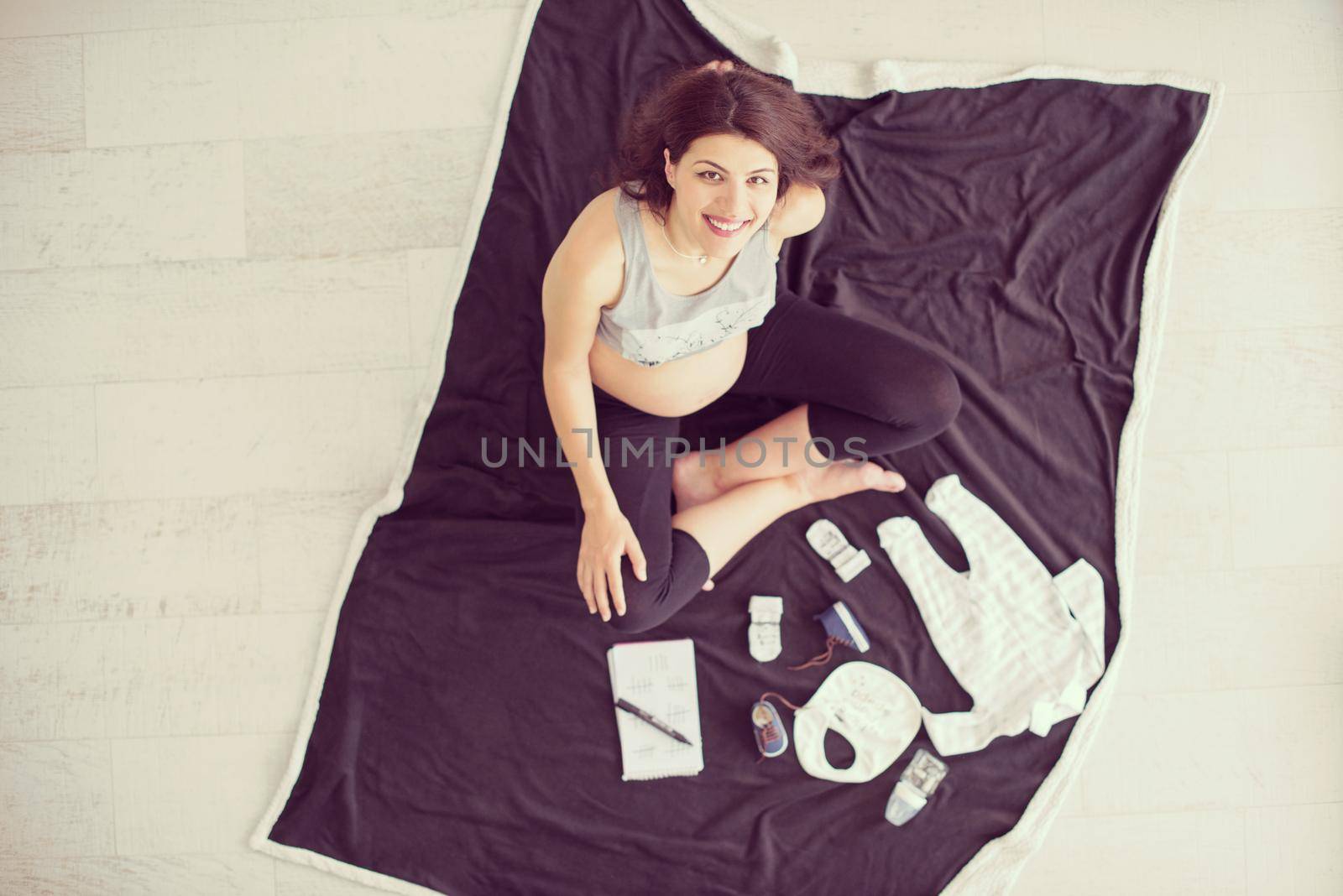 top view of pregnant woman checking list of baby clothes by dotshock