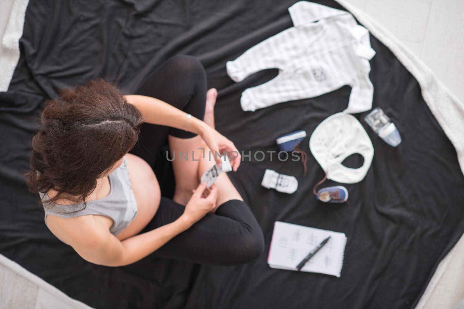 a pregnant woman at home on the floor checking list of baby clothes preparing for going to maternity hospital top view.Pregnancy, birth concept