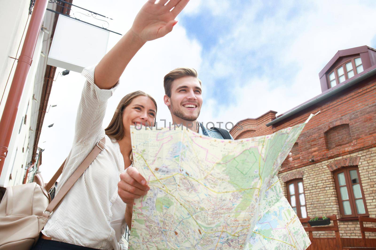 Happy couple walking outdoors sightseeing and holding a map.