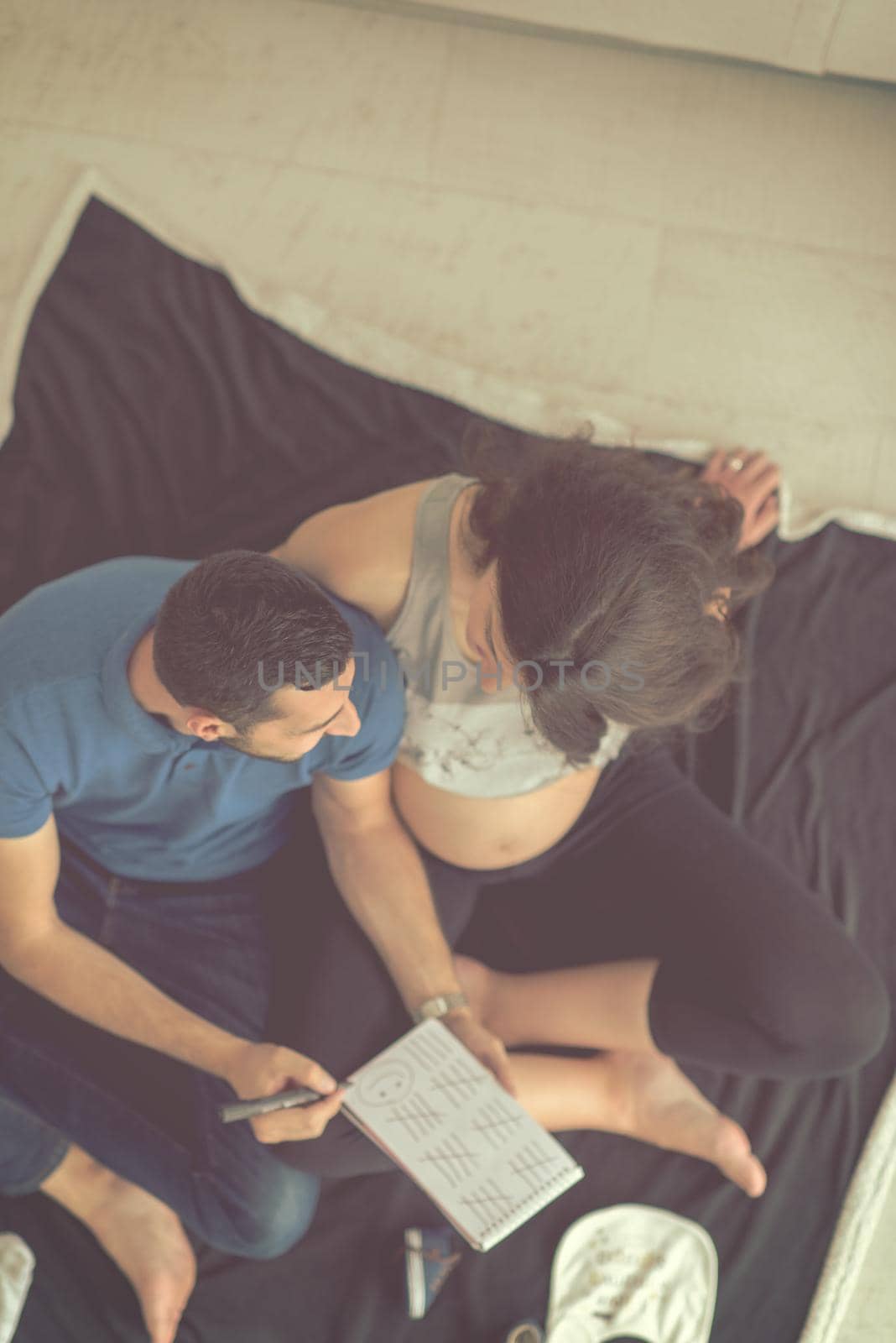 top view of a happy pregnant couple checking a list of things for their unborn baby at home on the floor