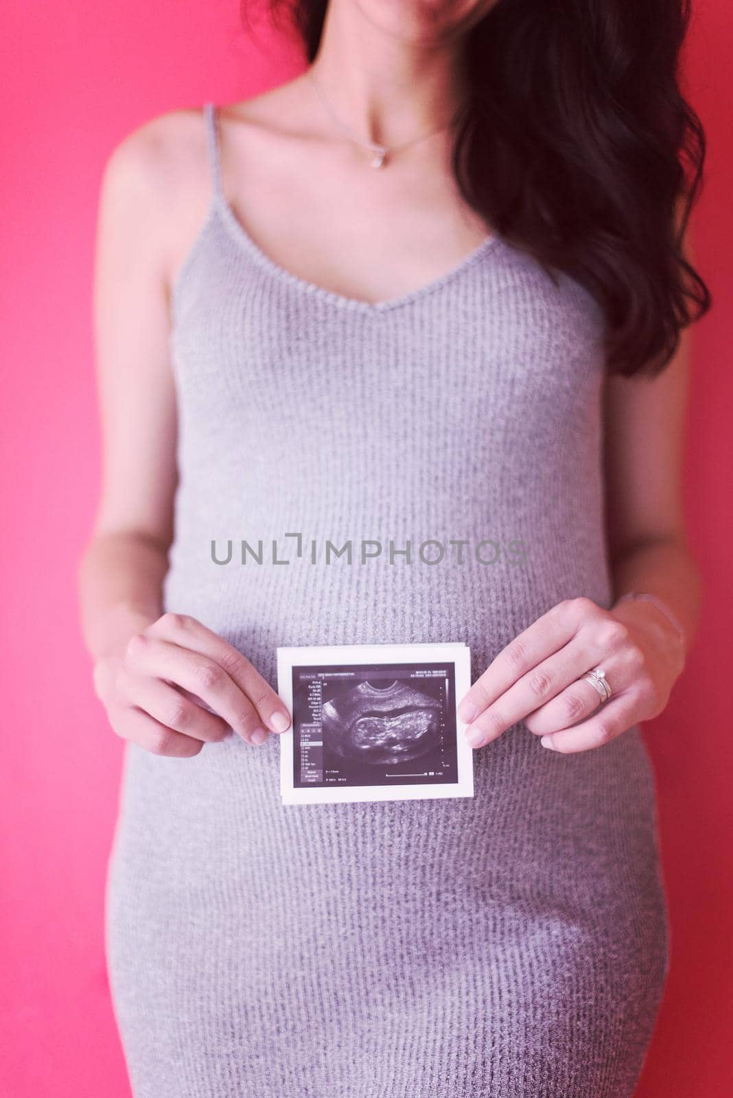 smiling pregnant woman showing ultrasound picture of her unborn baby isolated on red background