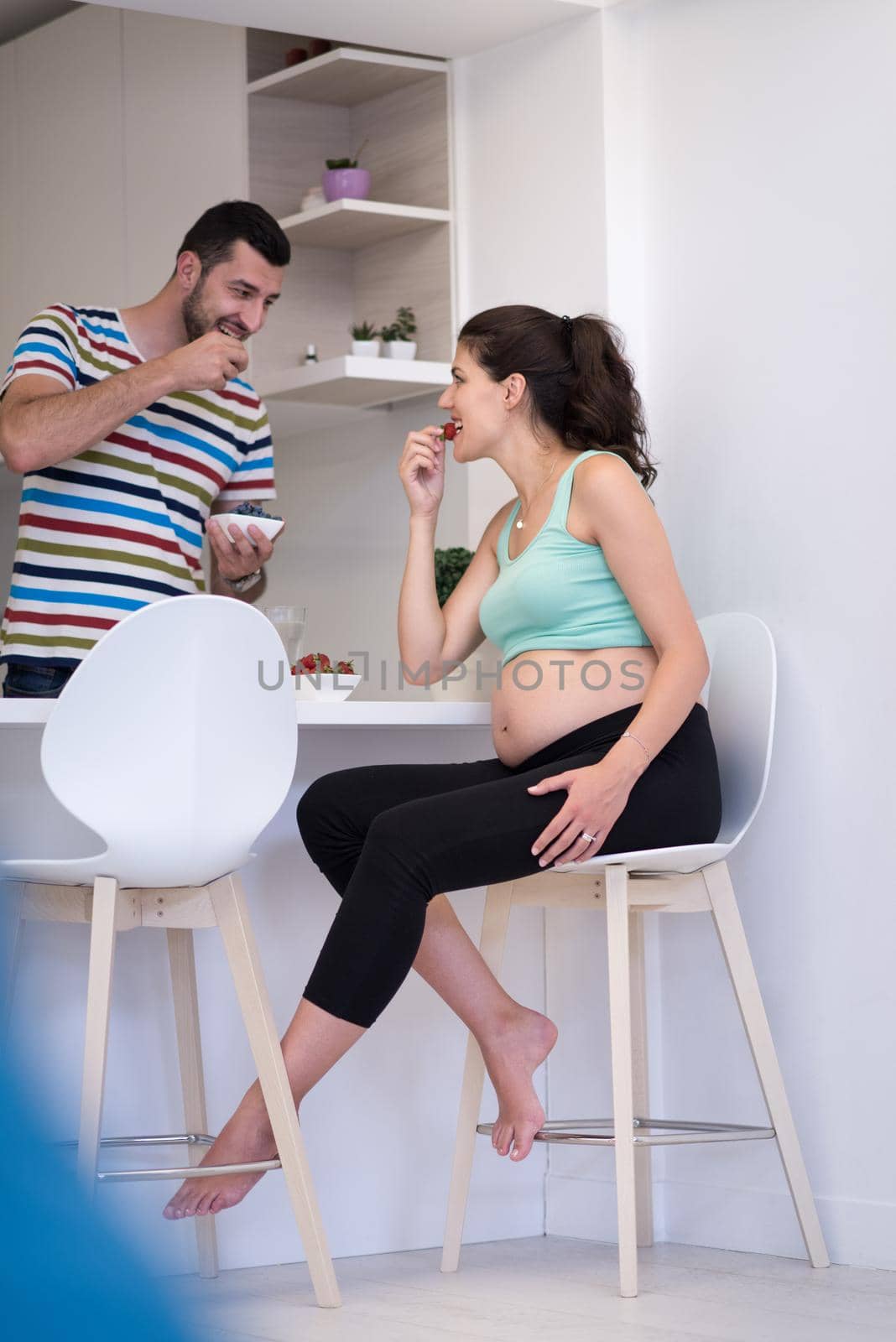 young pregnant couple eating strawberries at kitchen, lifestyle healthy pregnancy happy life concept