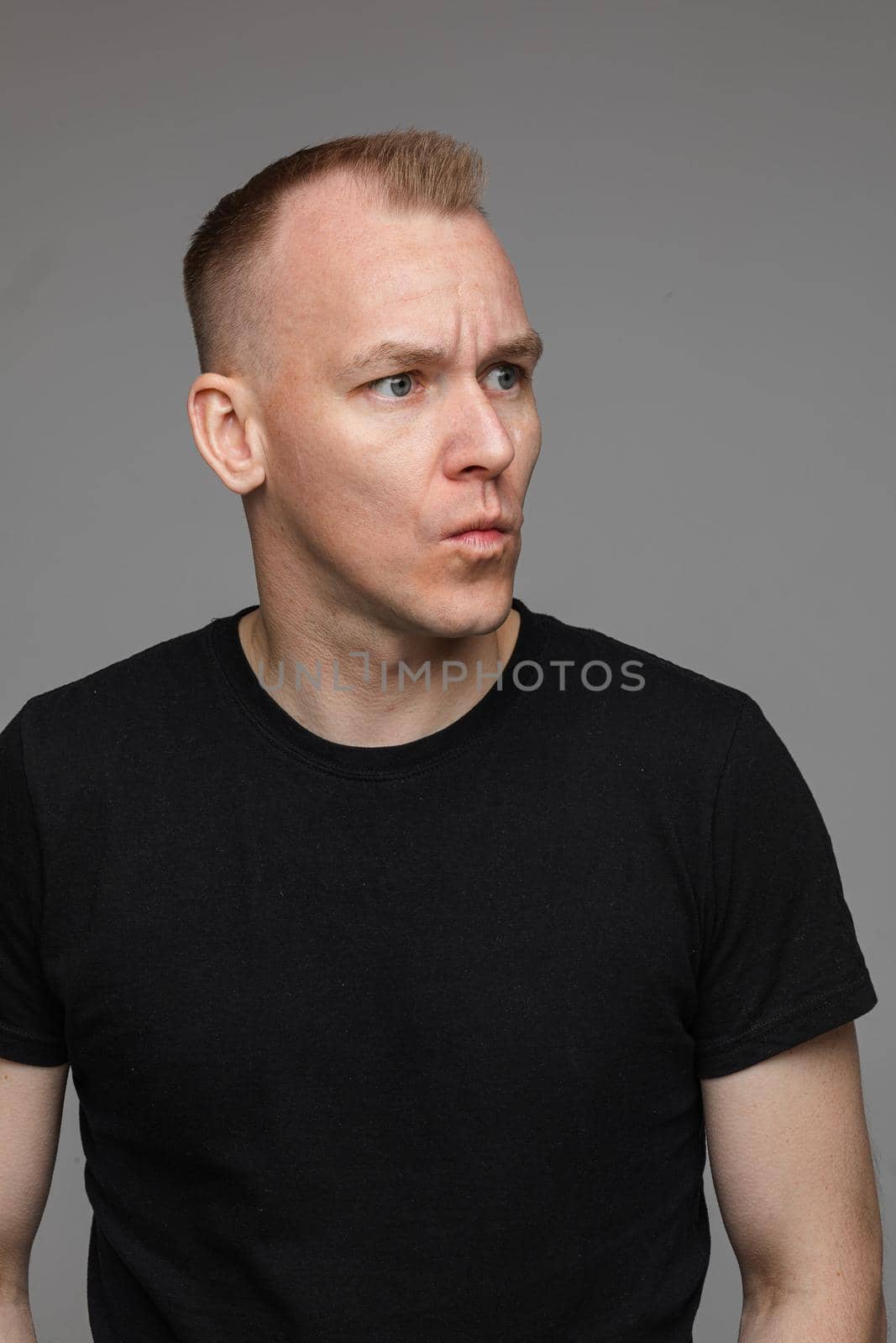 adult caucasian man in black t-shirt and short hair looks aside and thinks