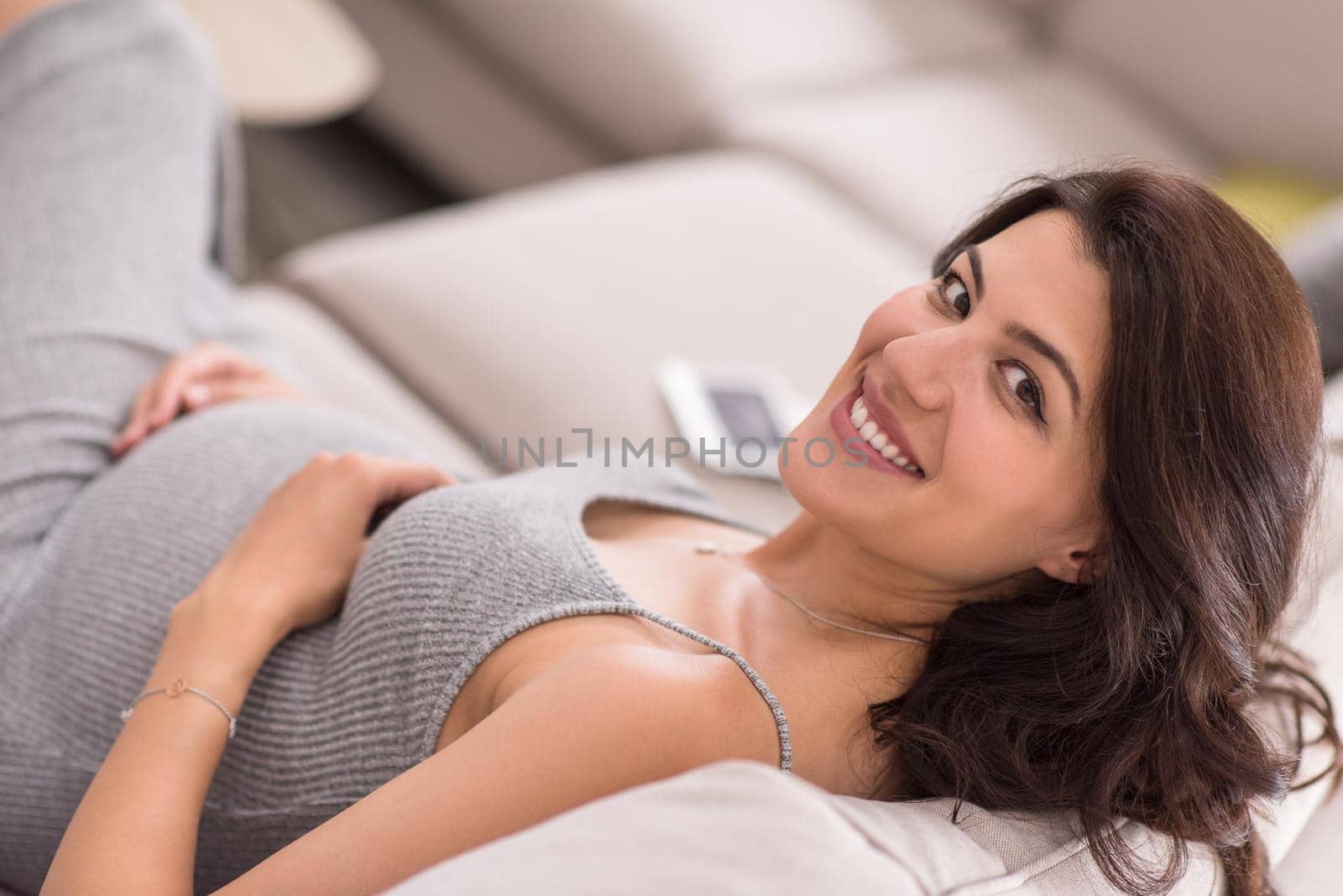 young happy pregnant woman keeping hand on belly while sitting on sofa at home
