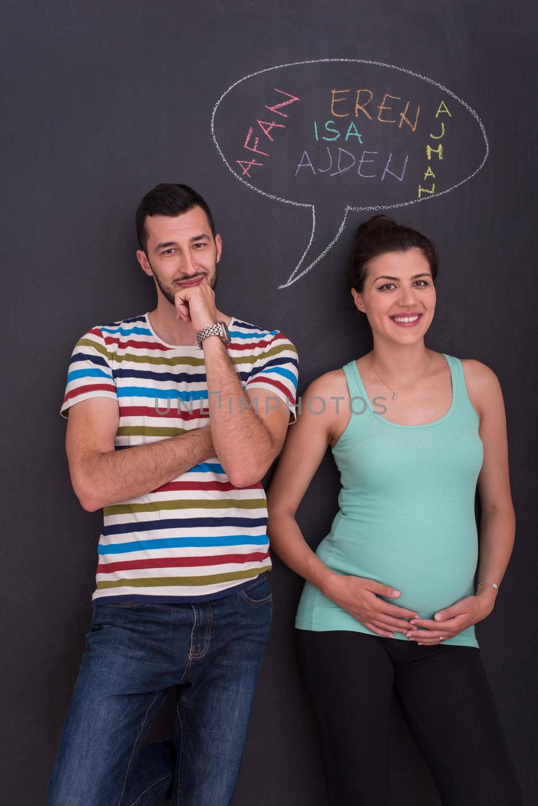 young pregnant couple thinking about names for their unborn baby and writing them on a black chalkboard