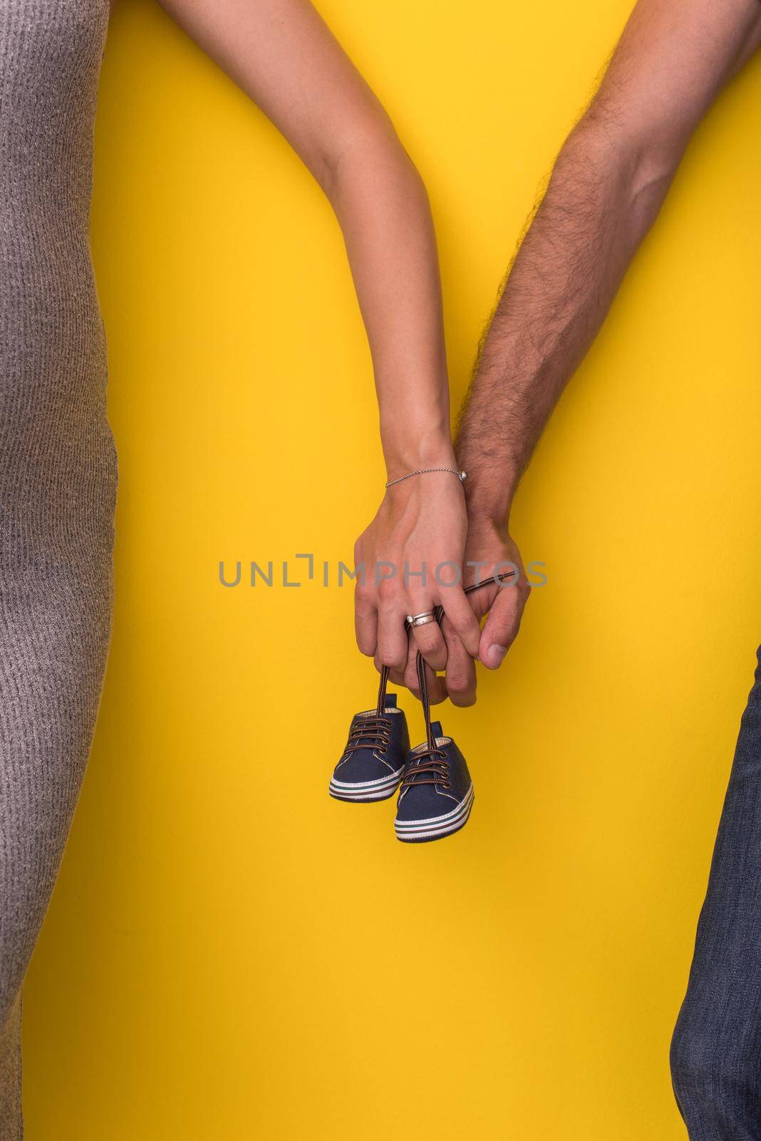 young  pregnant couple holding newborn baby shoes isolated on yellow background,family and parenthood concept