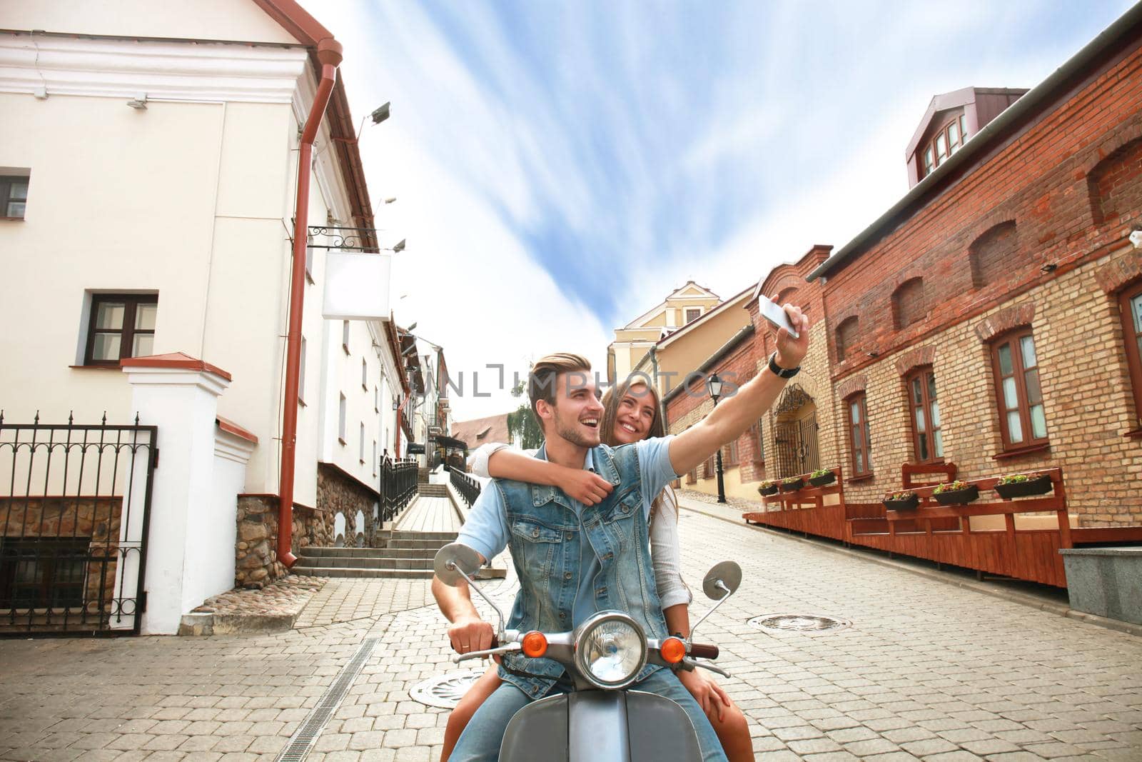 Happy couple on scooter making selfie photo on smartphone outdoors