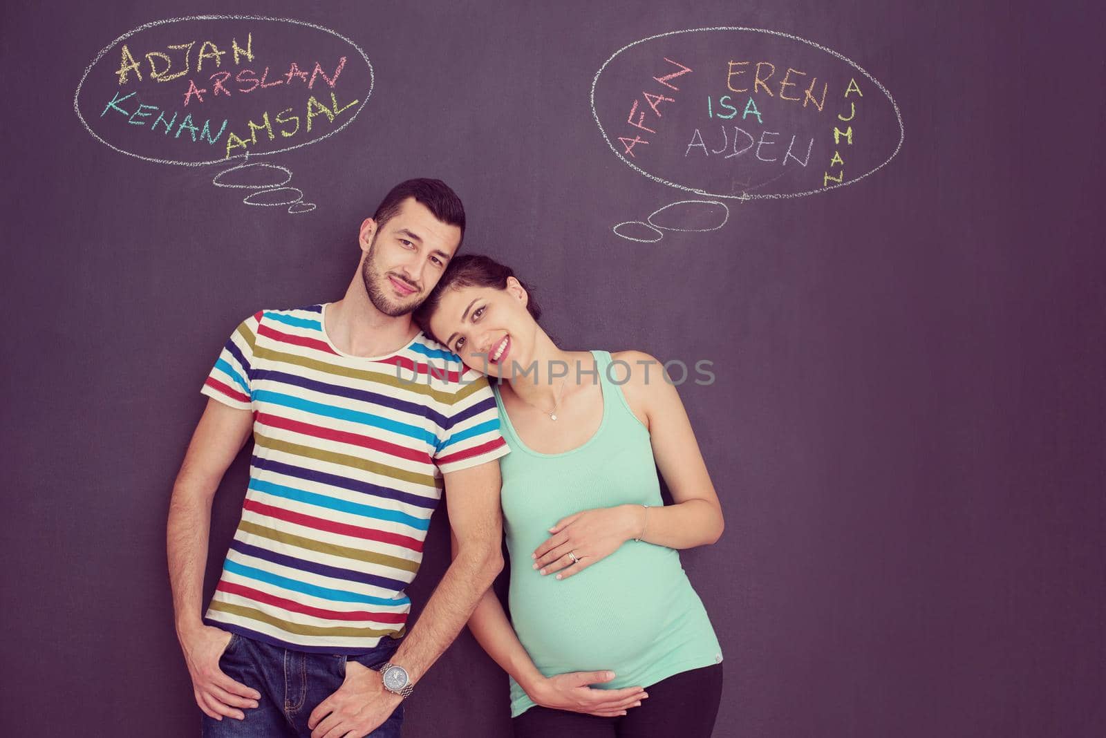 young pregnant couple thinking about names for their unborn baby and writing them on a black chalkboard