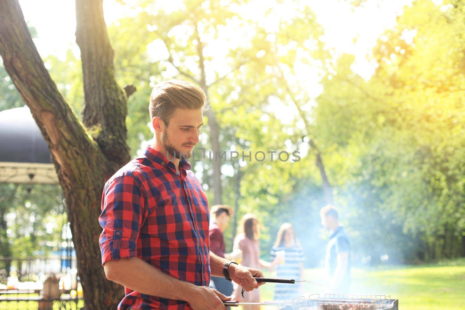 Handsome happy male preparing barbecue outdoors for friends. by tsyhun