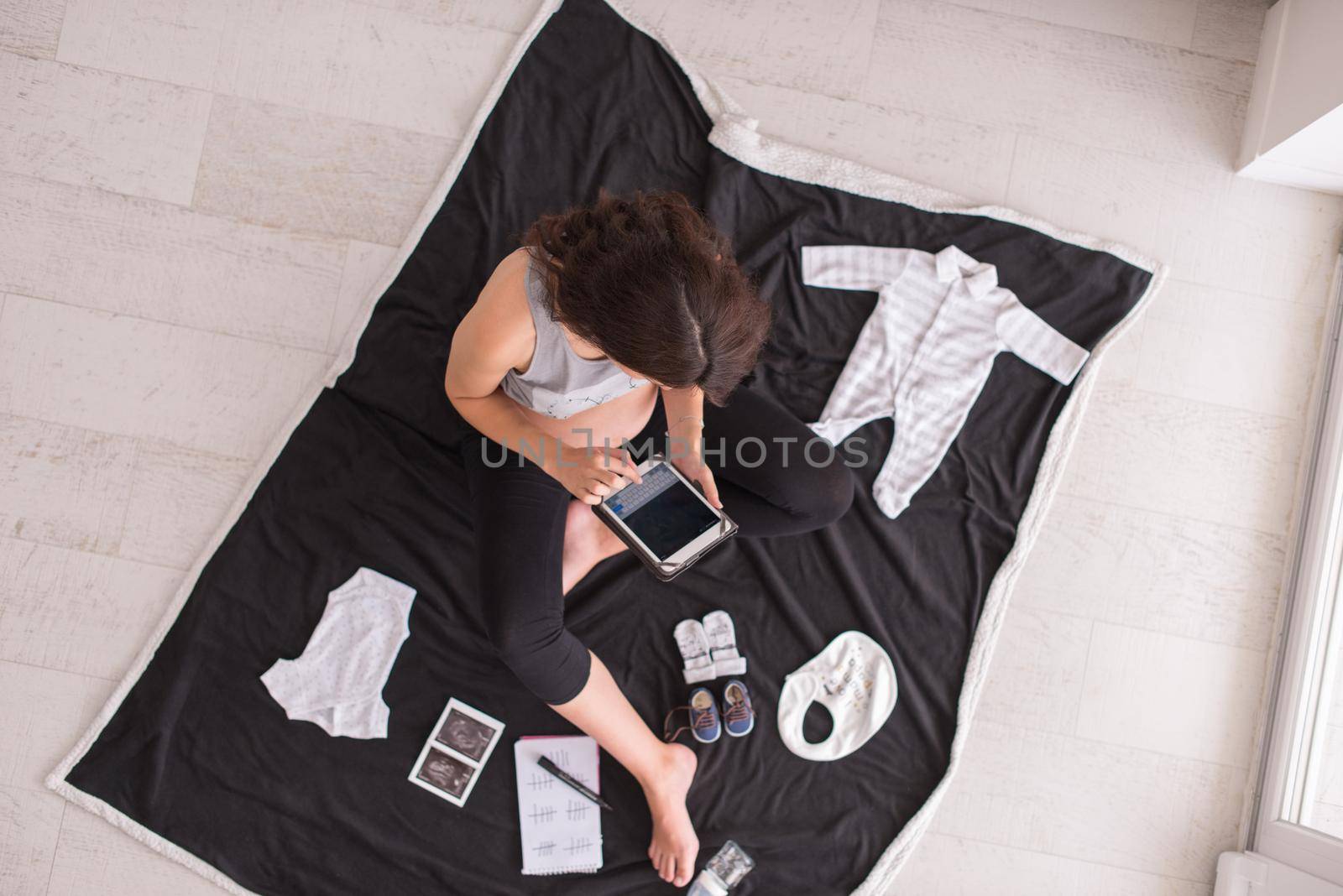 top view of pregnant woman checking list of baby clothes by dotshock