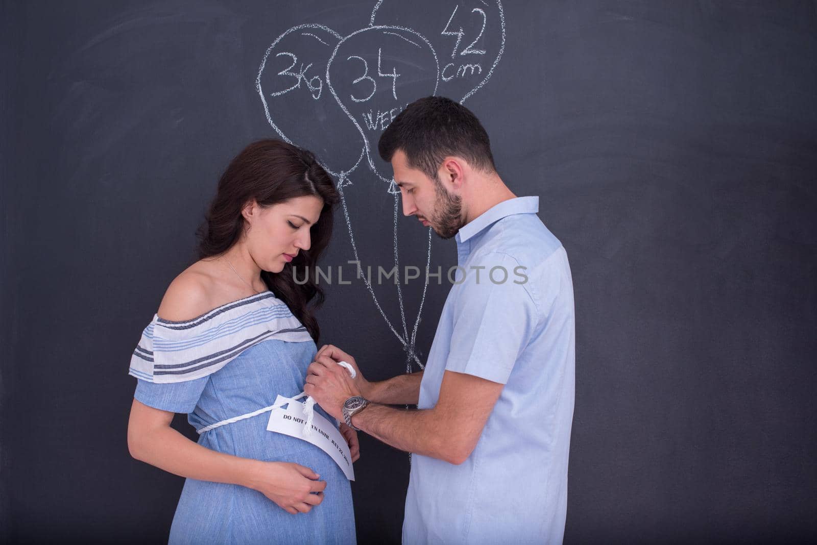 Conceptual photo of pregnant couple drawing their imaginations about the future life with children on chalk board