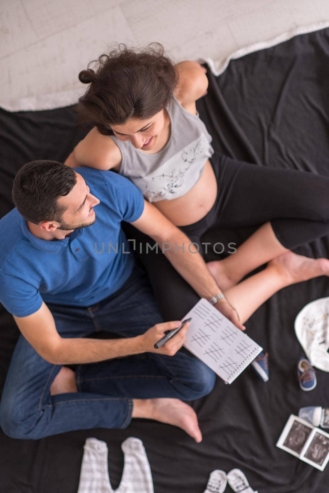 top view of a happy pregnant couple checking a list of things for their unborn baby at home on the floor