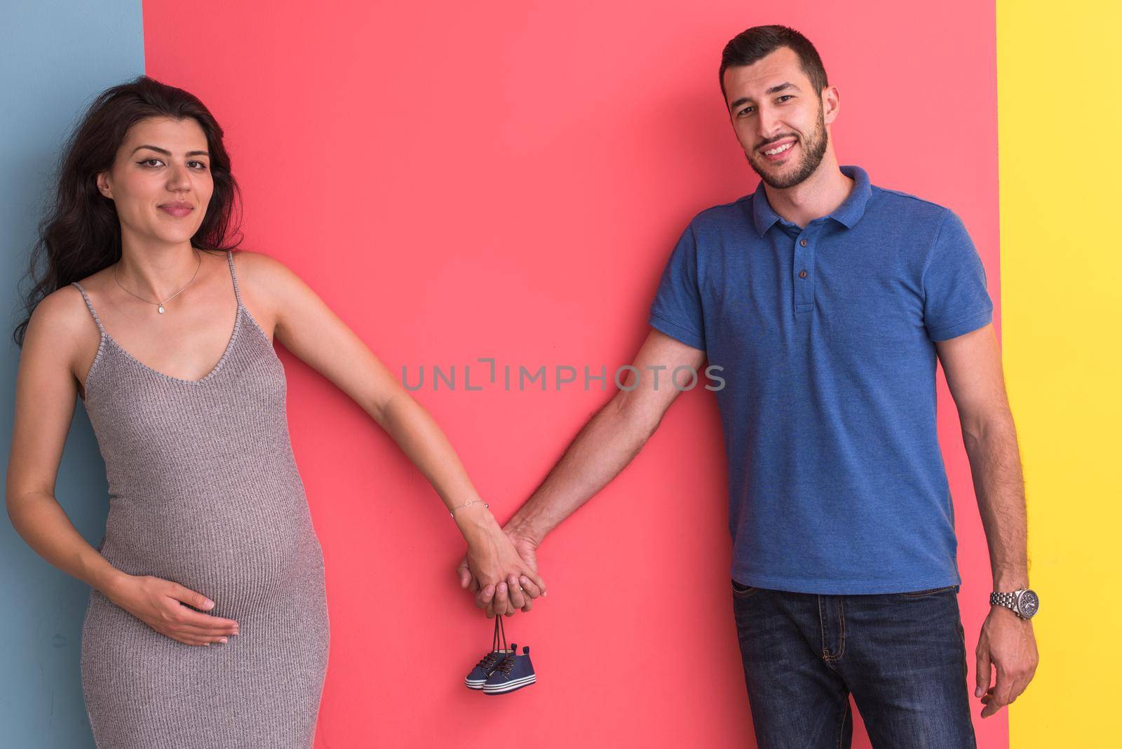 young pregnant couple holding newborn baby shoes isolated on colorful background,family and parenthood concept