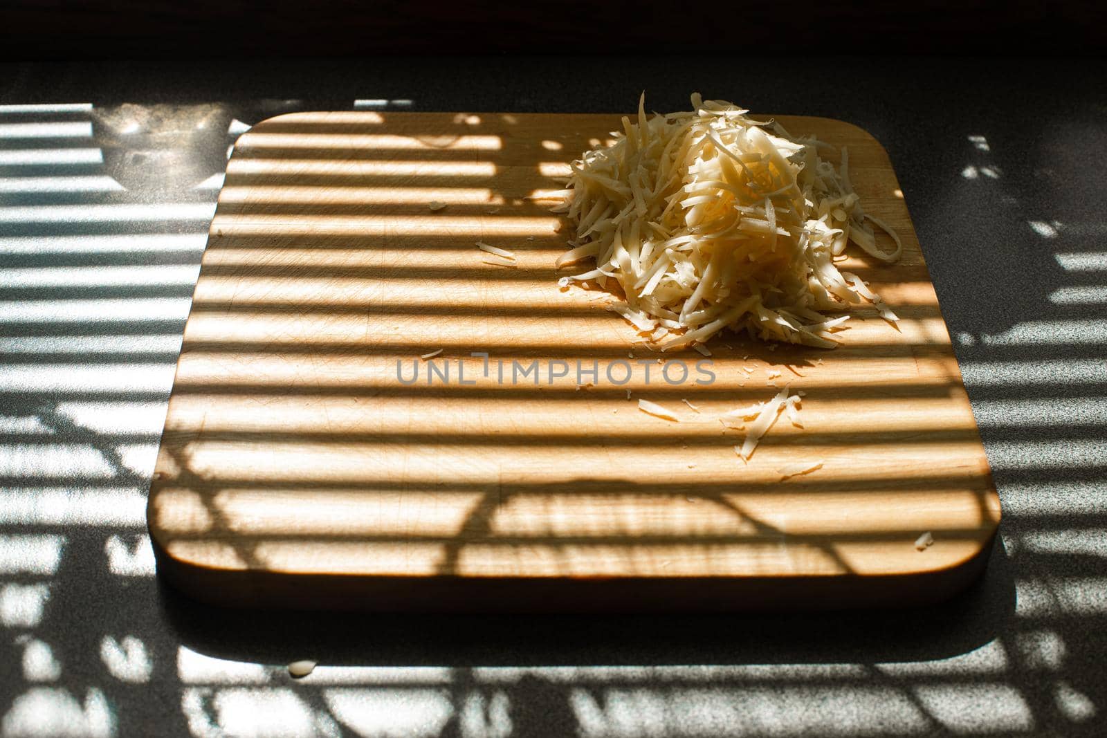 A small pile of grated fresh cheese lies on a wooden board in the kitchen by StudioLucky