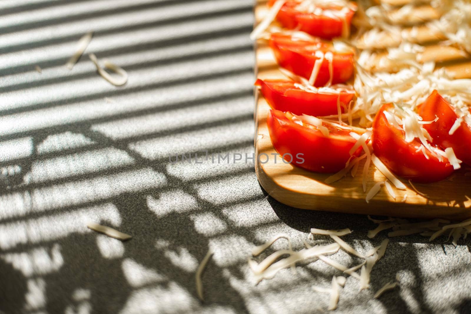 A small pile of grated fresh cheese and red tomatoes lies on a wooden board in the kitchen.