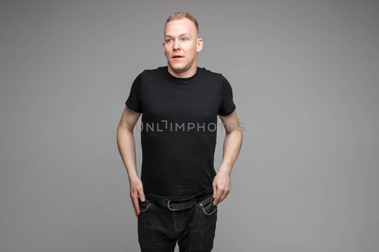 picture of caucasian male wearing a black t-shirt and jeans on grey background