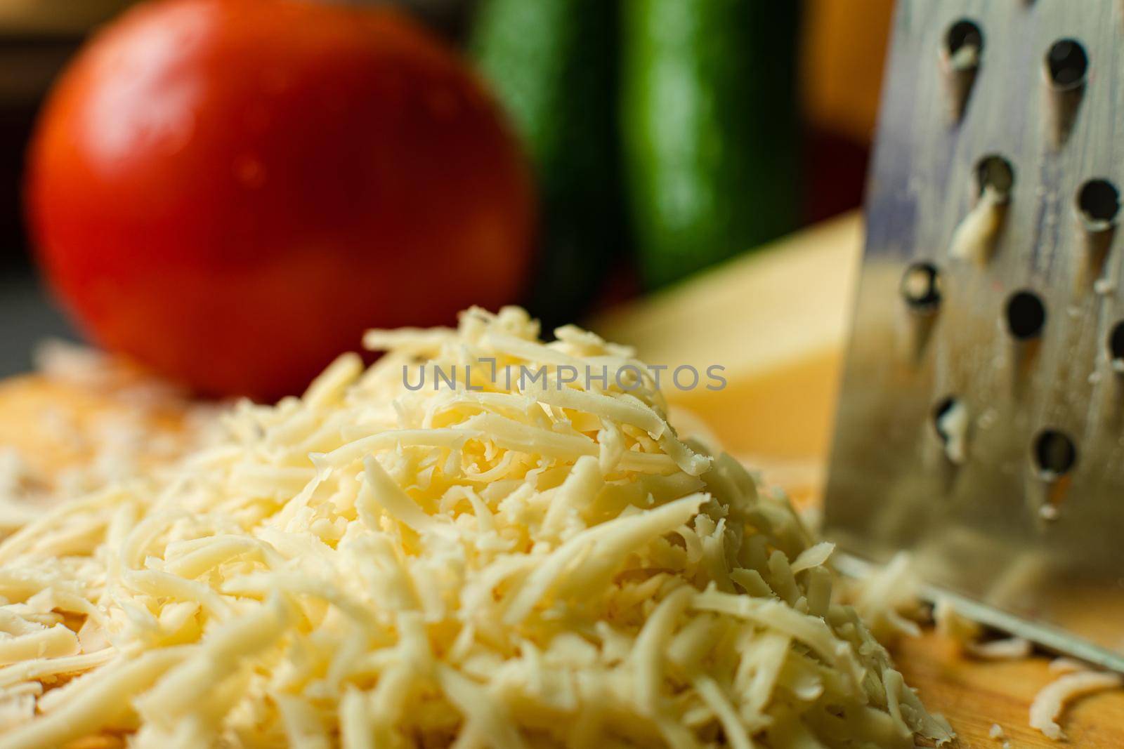 Picture of metal kitchen grater with oval holes on it on the kitchen table with cheese