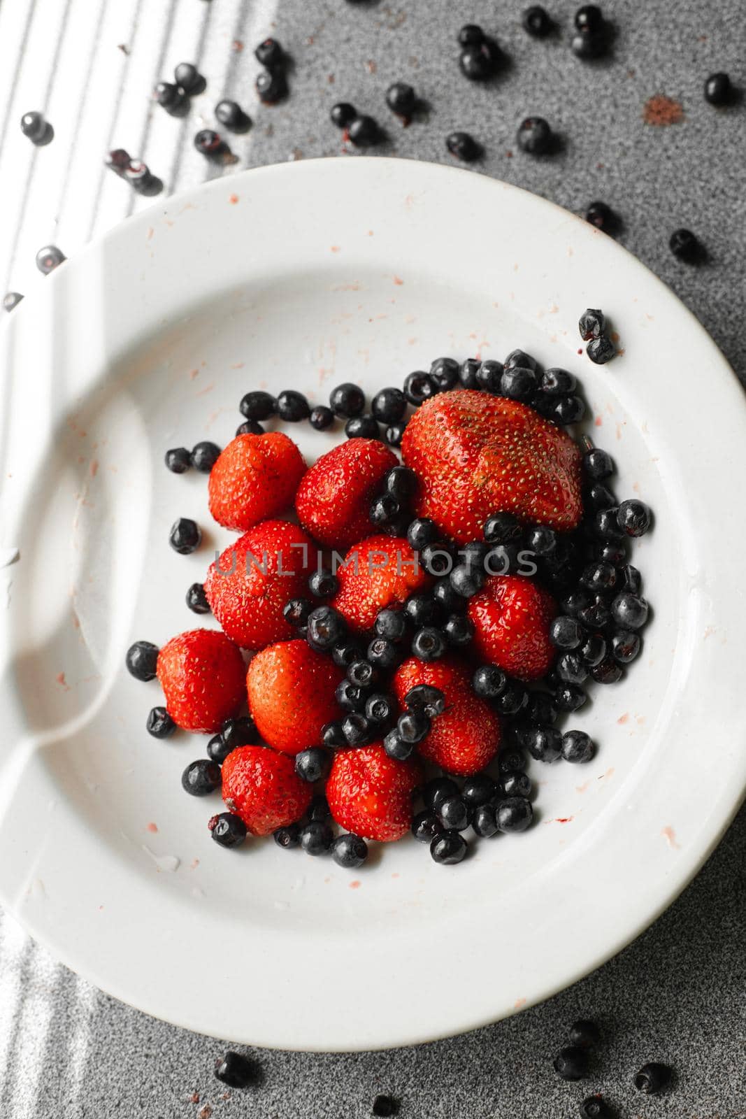 Many juicy fresh ripe red berries and blackberries lie in a white ceramic plate on the table by StudioLucky