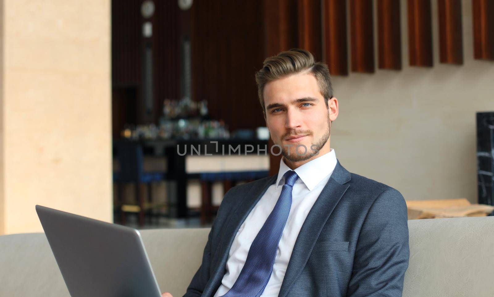 Young businessman working on laptop, sitting in hotel lobby waiting for someone