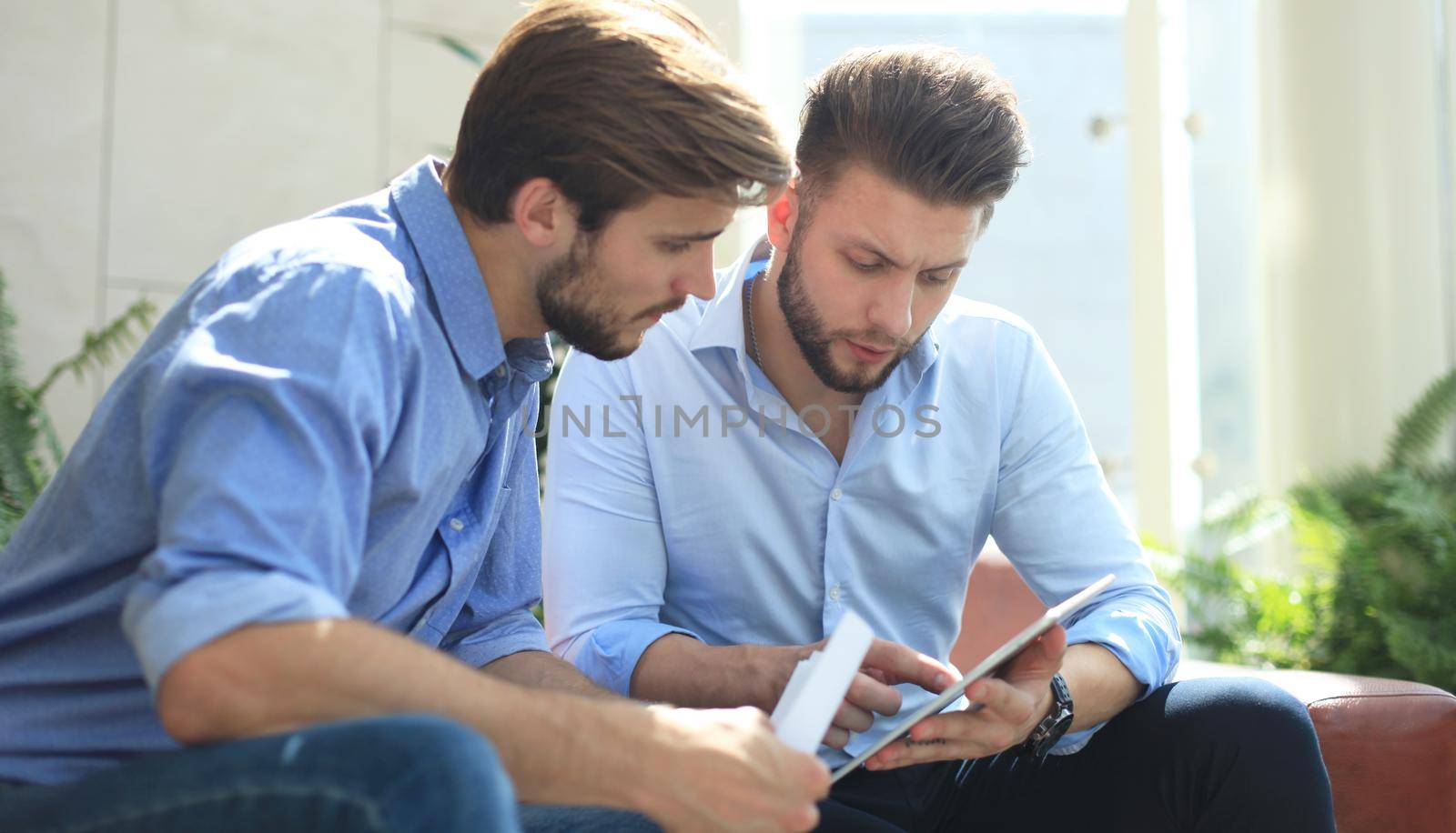Mature businessman using a digital tablet to discuss information with a younger colleague in a modern business office by tsyhun