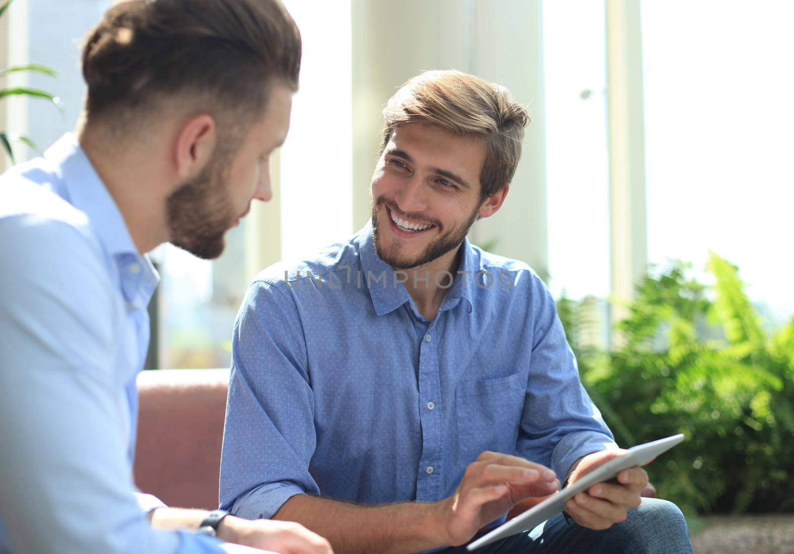 Mature businessman using a digital tablet to discuss information with a younger colleague in a modern business office by tsyhun