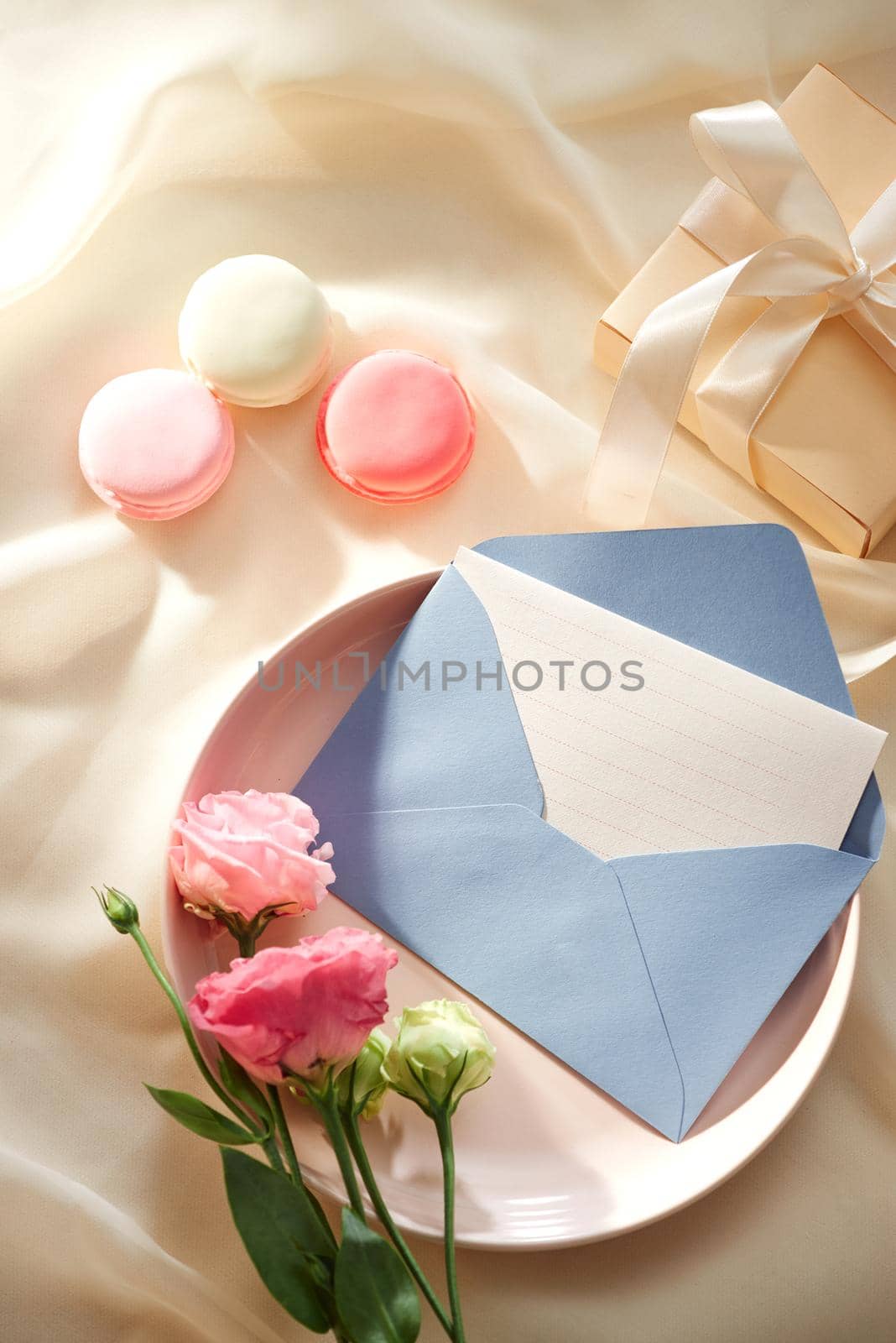 Envelope wih blank paper card on the light fabric background with lusianthus and gift box, top view by makidotvn