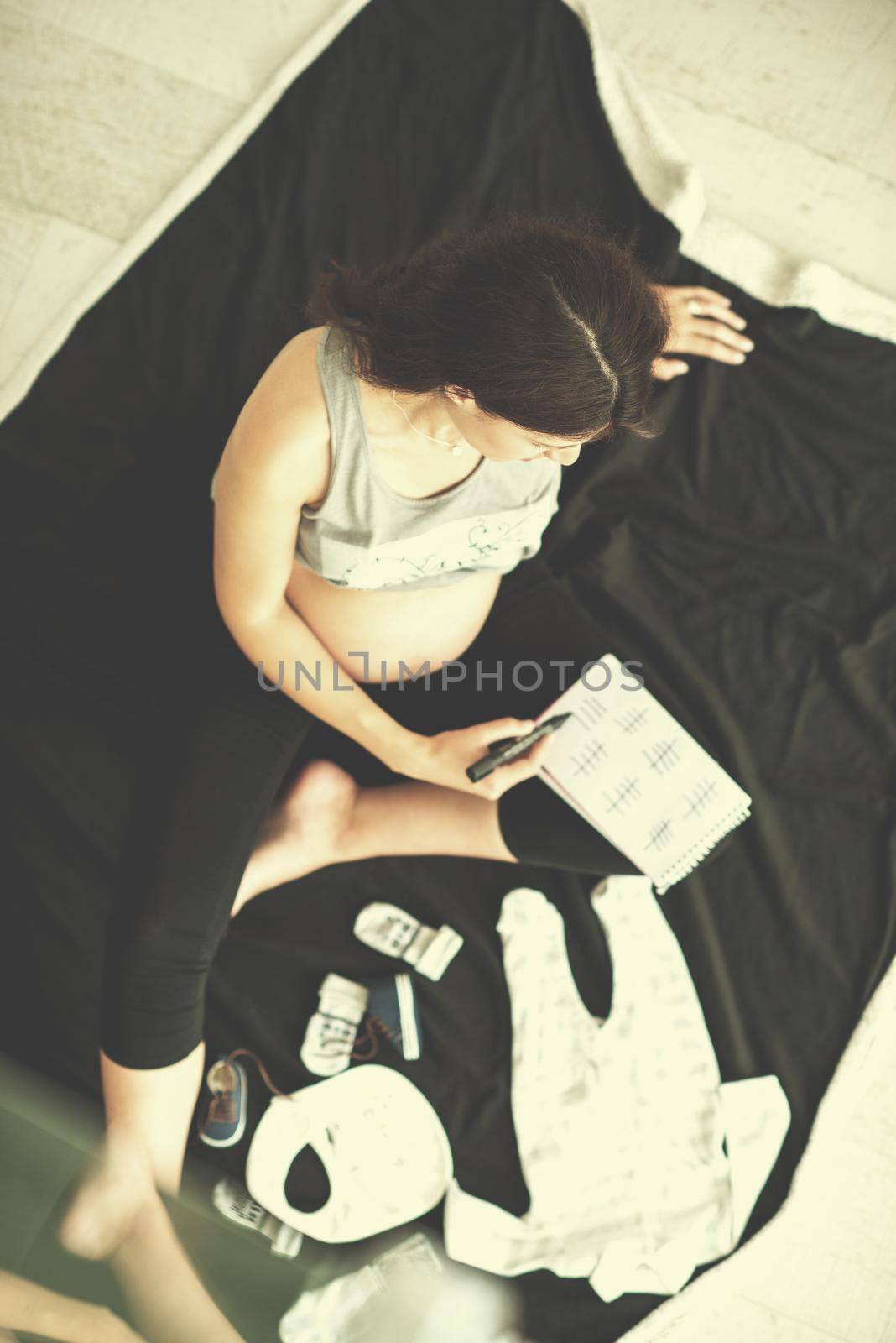 a pregnant woman at home on the floor checking list of baby clothes preparing for going to maternity hospital top view.Pregnancy, birth concept