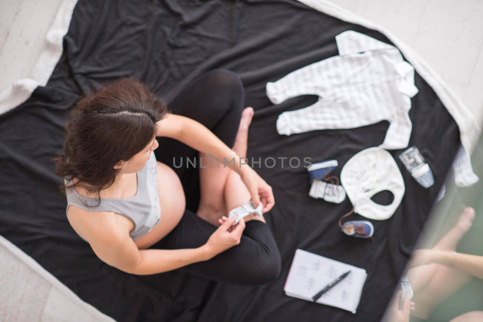 a pregnant woman at home on the floor checking list of baby clothes preparing for going to maternity hospital top view.Pregnancy, birth concept