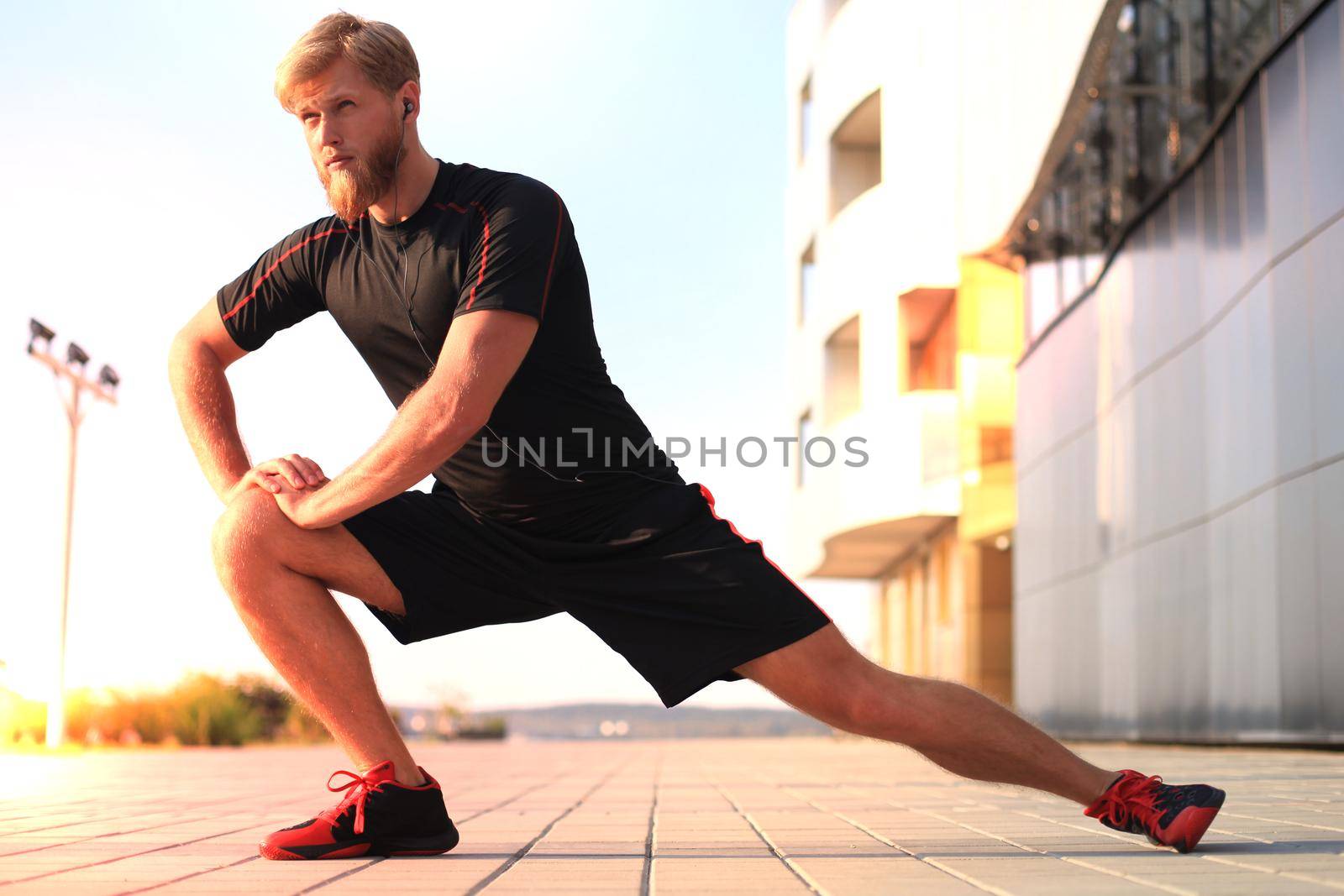 Handsome young man doing stretching exercises before running while standing outdoors