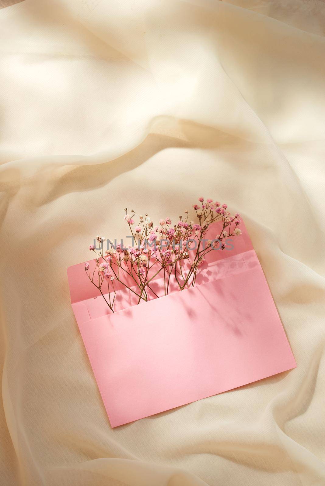 Pink envelope with a spring flower arrangement. Flat lay, top view