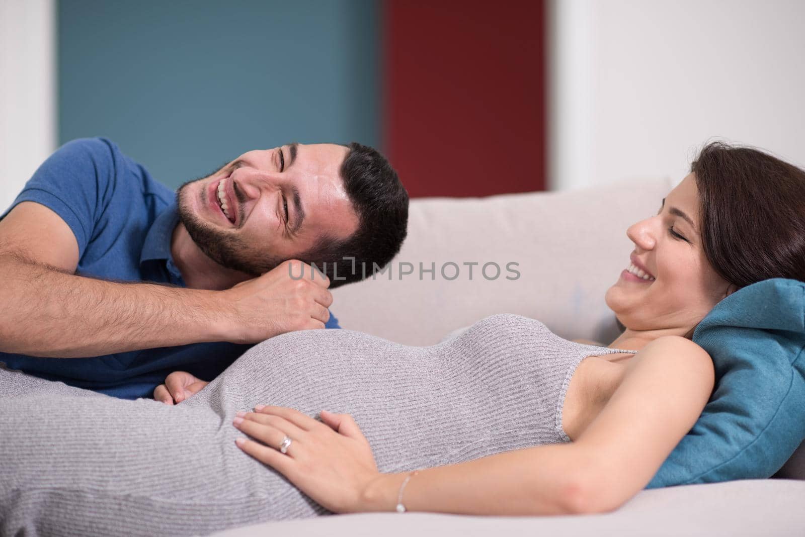 Happy future dad listening the belly of his pregnant wife while relaxing on sofa at home