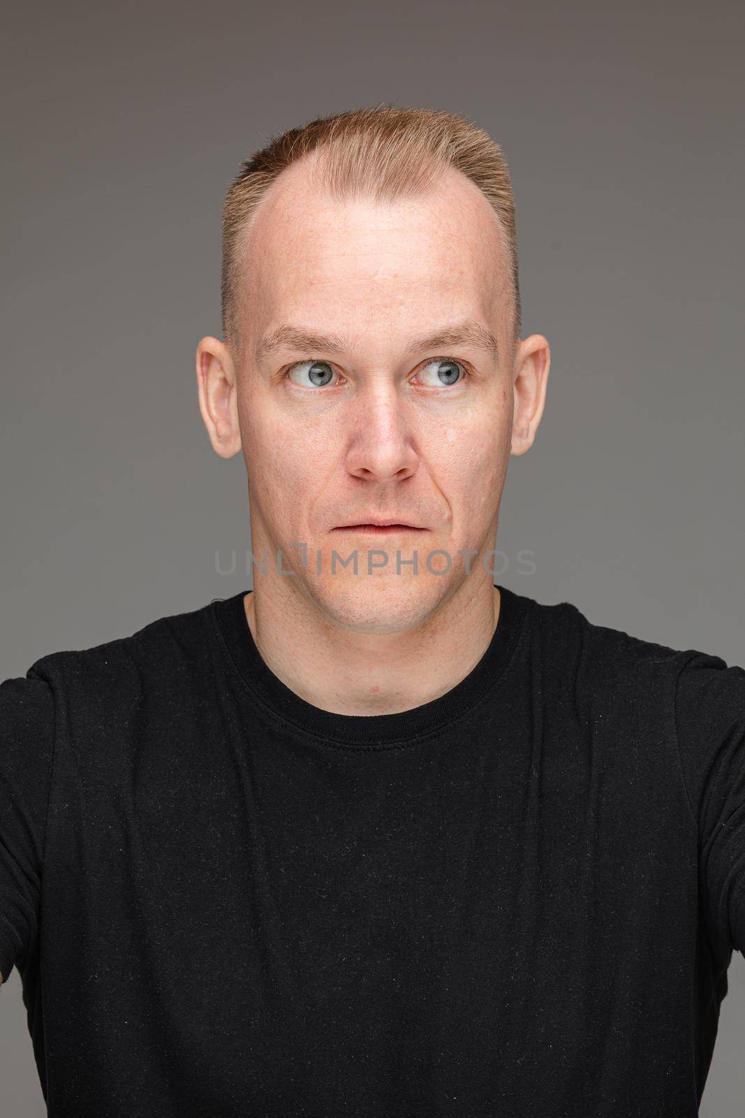 Portrait of a blond Caucasian man in black t-shirt looking away with his eyes wide-open showing surprise or shock.