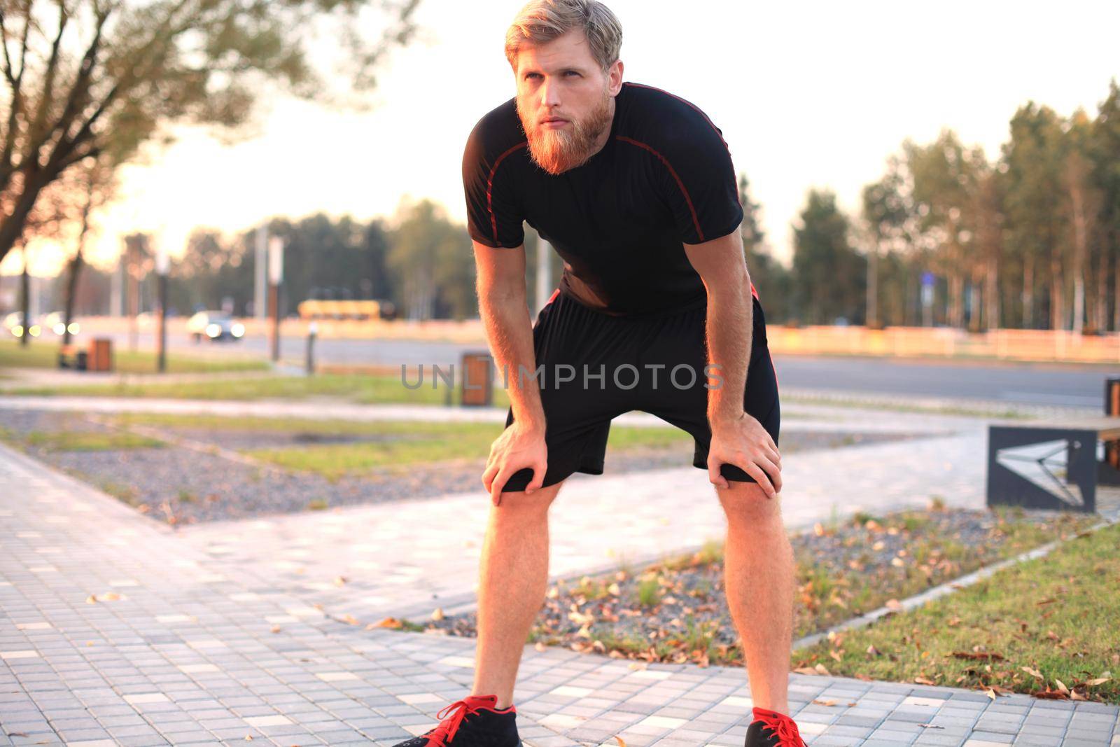 Handsome young man after run resting after jog at the park at sunset or sunrise