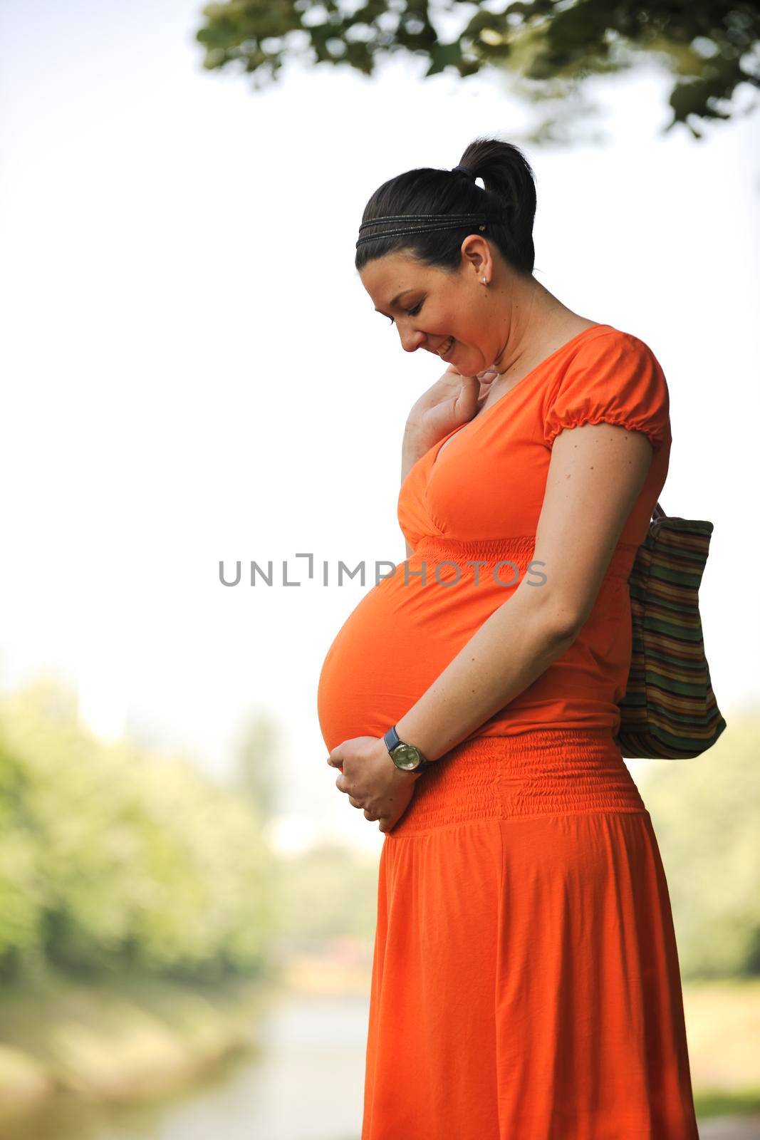 beautiful young happy pregnant woman outdoor in bright nature in orange dress