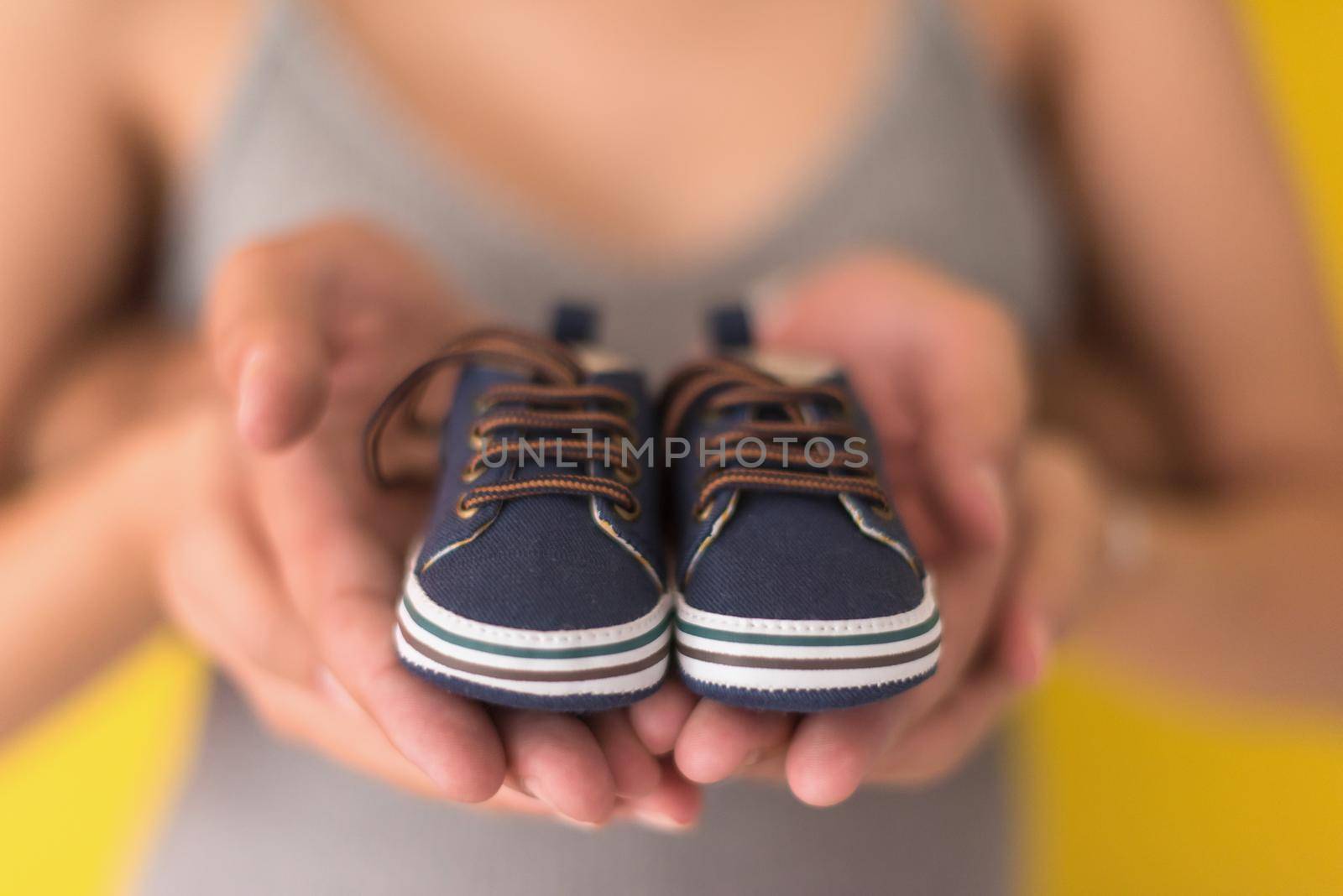 young  pregnant couple holding newborn baby shoes isolated on yellow background,family and parenthood concept