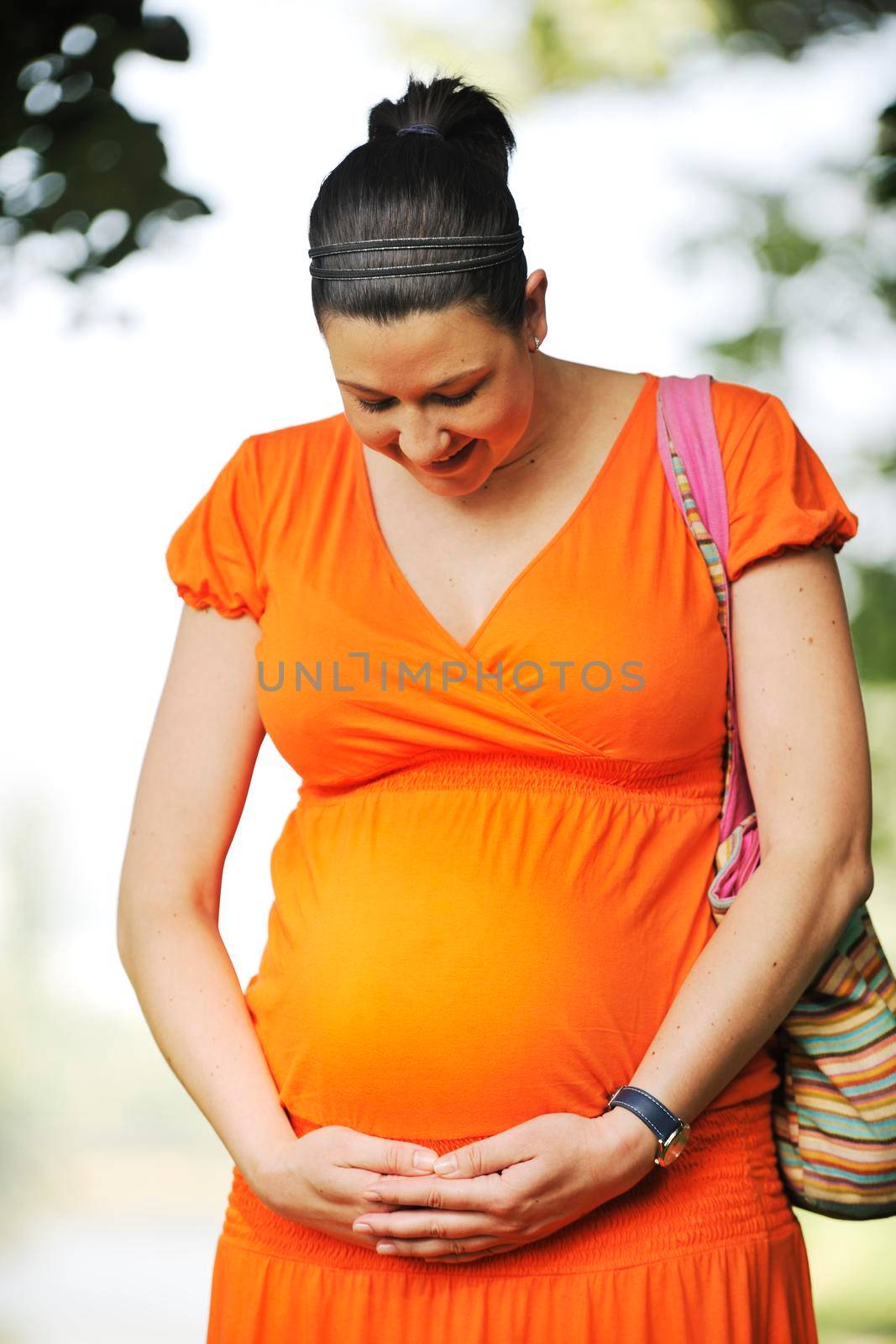 beautiful young happy pregnant woman outdoor in bright nature in orange dress