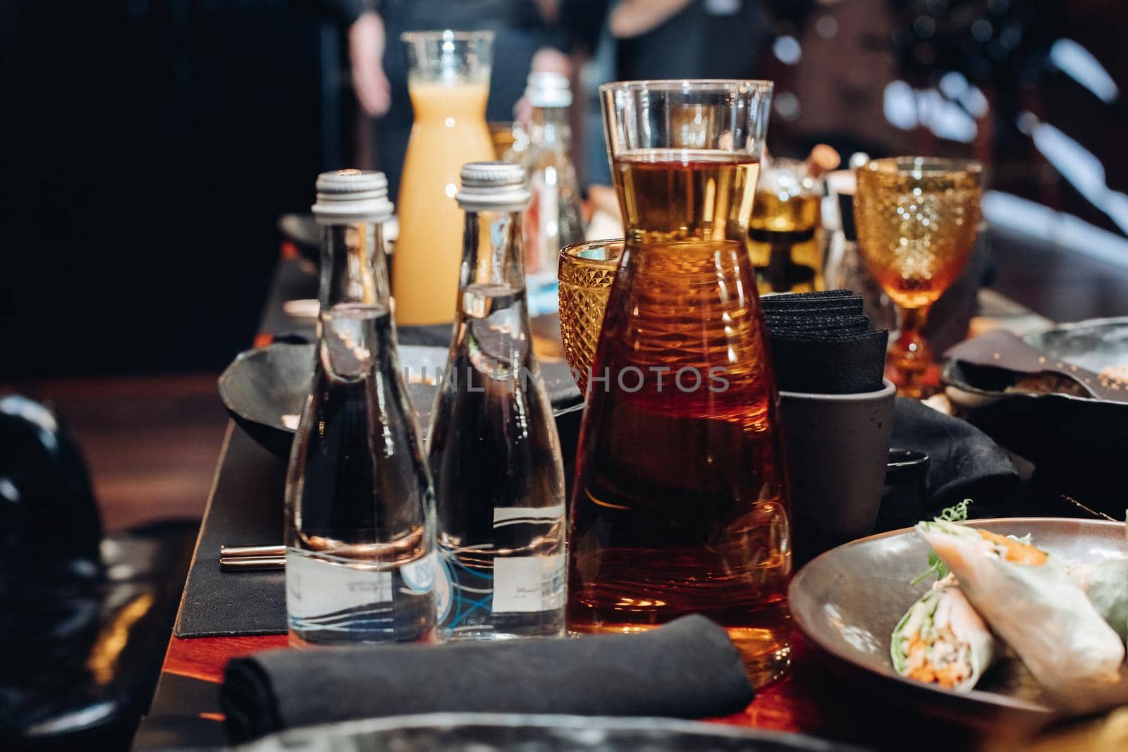 Stock photo of full glass bottles of water and jar of pure still water on table with served food at banquet.