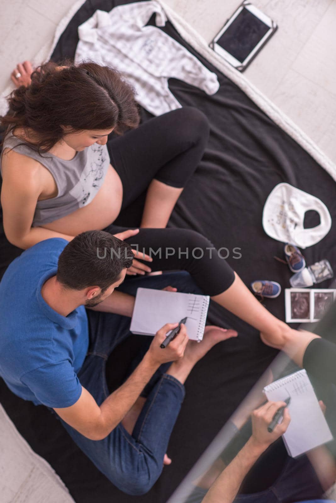 top view of a happy pregnant couple checking a list of things for their unborn baby at home on the floor