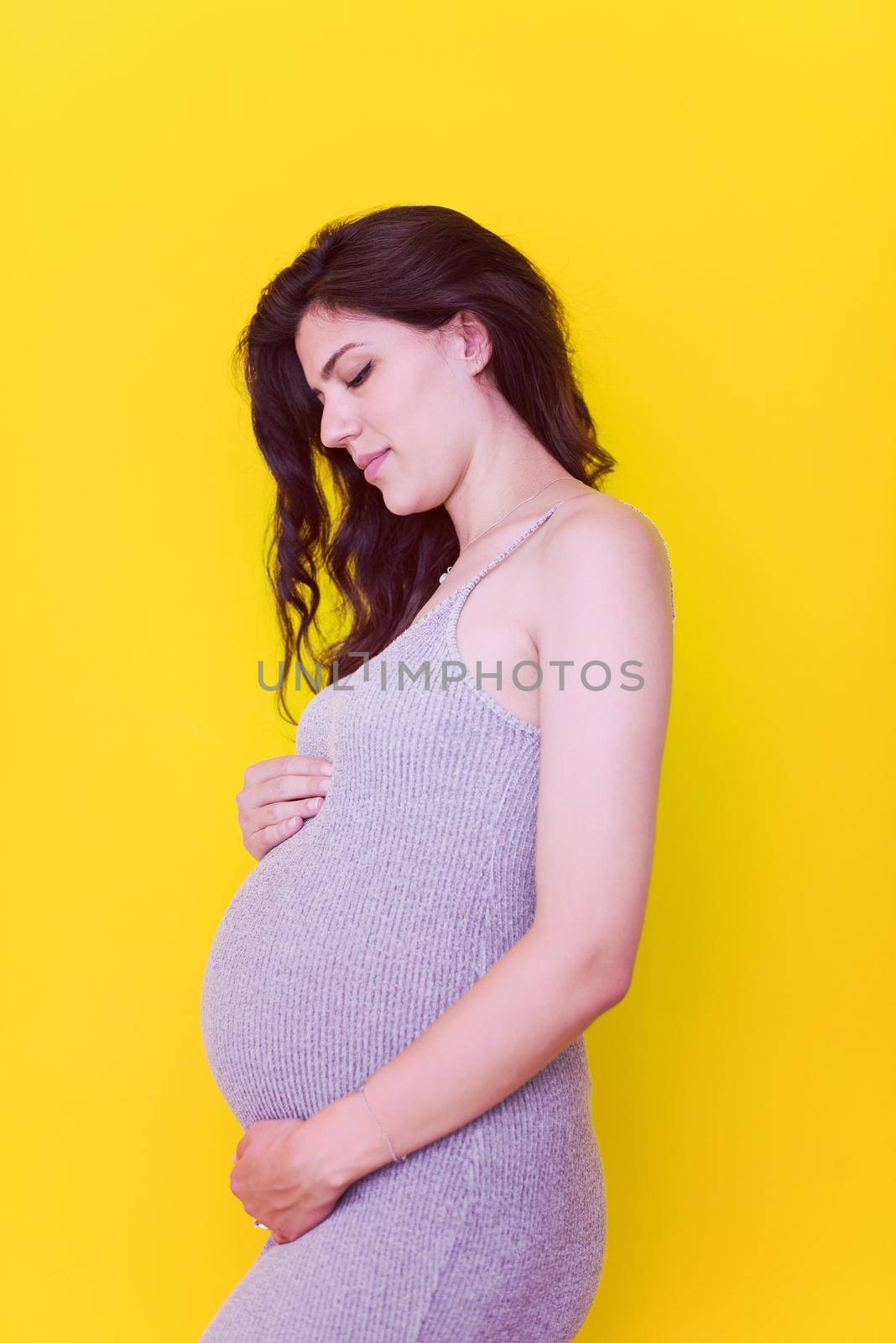 Portrait of happy pregnant woman with hands on belly isolated over yellow background