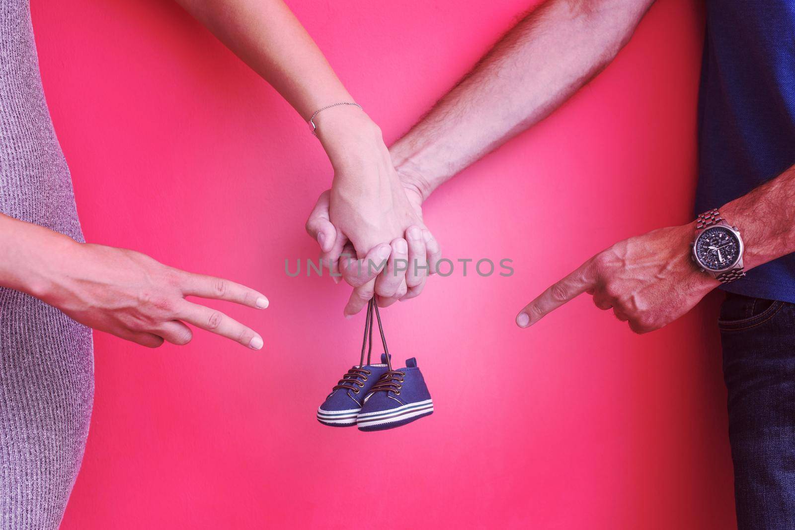 young  pregnant couple holding newborn baby shoes isolated on red background,family and parenthood concept
