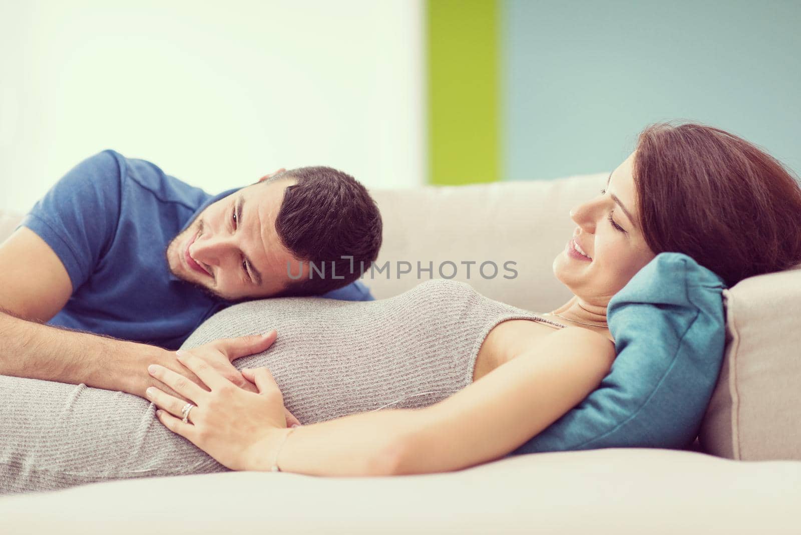 Happy future dad listening the belly of his pregnant wife while relaxing on sofa at home