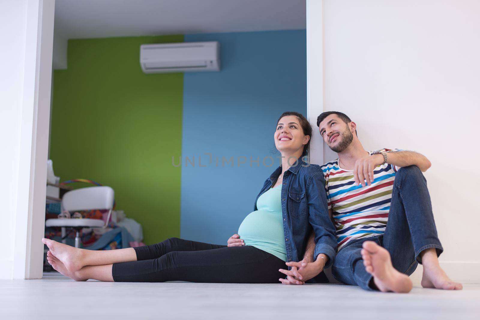 happy pregnant couple holding their hands while sitting on the floor at home