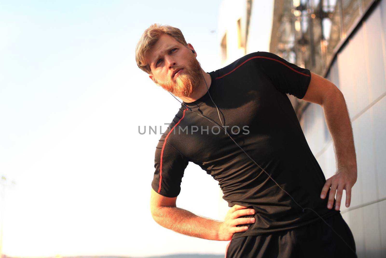 Handsome young man doing stretching exercises before running while standing outdoors