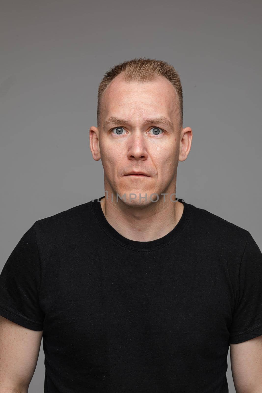 portrait of caucasian man in black t-shirt looks aside from the camera isolated on grey background by StudioLucky