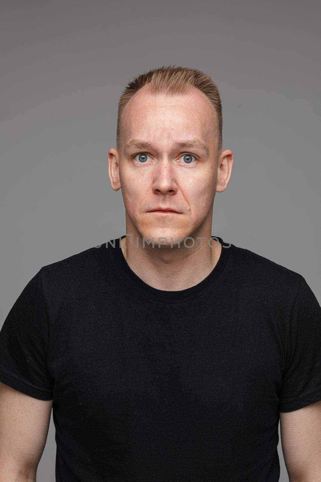 Studio portrait of adult Caucasian man with blond short hair in black t-shirt looking at camera with worried face. Concept of concern.